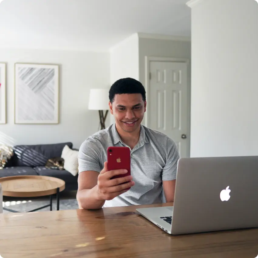 A man at the front of a laptop holding a phone